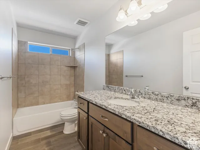 Hall bathroom featuring a vanity with granite countertop, wood-finish cabinetry, tile-surround tub, and wood-finish tile flooring