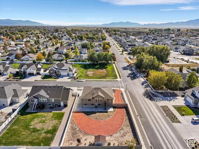 Aerial perspective of a residential property featuring a large curbed landscape area, a concrete patio, storage shed, and surrounding mountain scenery