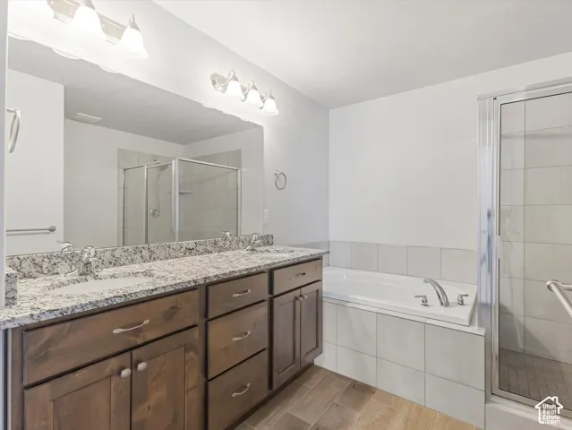 Primary bathroom with dual-sink vanity with granite countertop, soaking tub, glass-enclosed shower, and wood-finish tile flooring