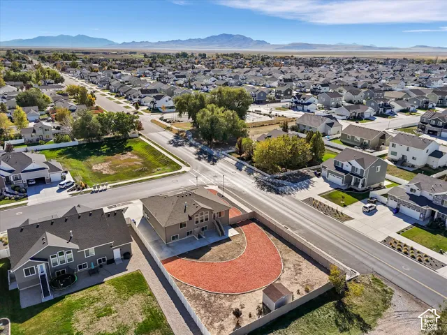 Aerial perspective featuring a residence with an asphalt shingle roof, fenced perimeter, a concrete driveway, and mountain backdrops