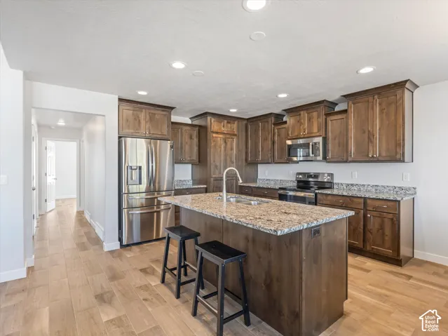 Kitchen featuring wood cabinetry, stone countertops, central island with an integrated sink, stainless steel appliances, and wood-finish flooring