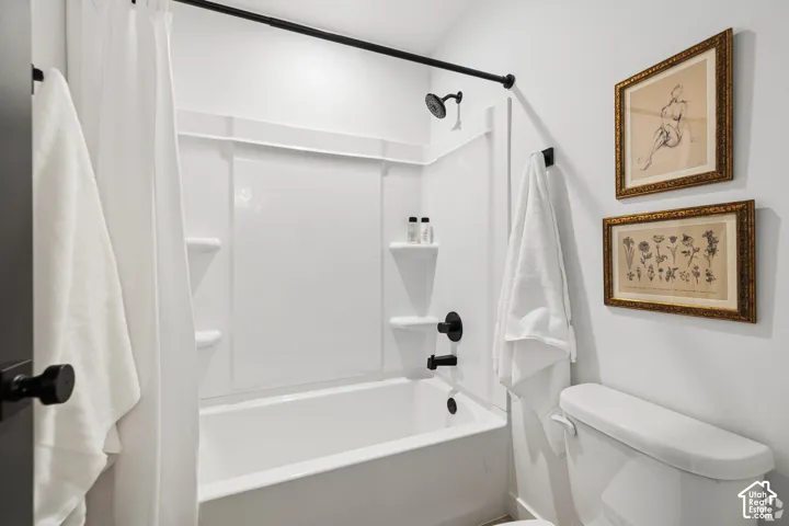 Bathroom featuring a white molded tub surround with integrated shelving, matte black plumbing fixtures, a matte black shower curtain rod, and a standard toilet