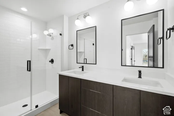 Dual-sink vanity with dark wood-finish cabinetry and quartz countertops, accompanied by a glass-enclosed shower with subway tile surround, matte black fixtures, and rectangular mirrors
