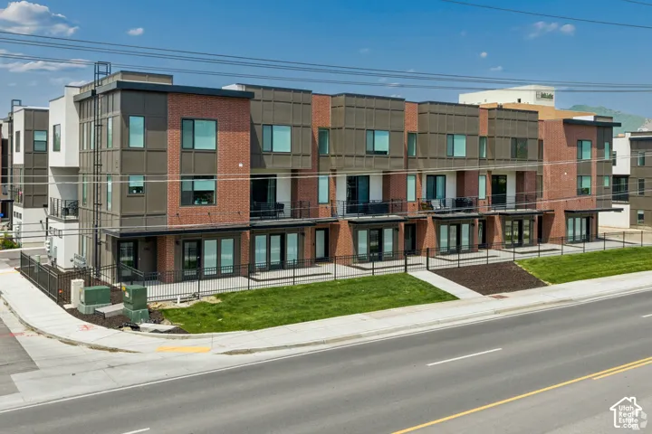 Multi-unit residential complex featuring brick and paneled siding, individual ground-level patios, second-story balconies with metal railings, and landscaped front lawn areas