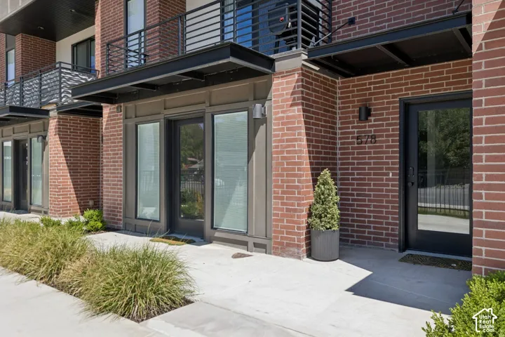 Multi-story brick exterior featuring black metal awnings, full-glass panel entry doors, and second-level balconies with black railing