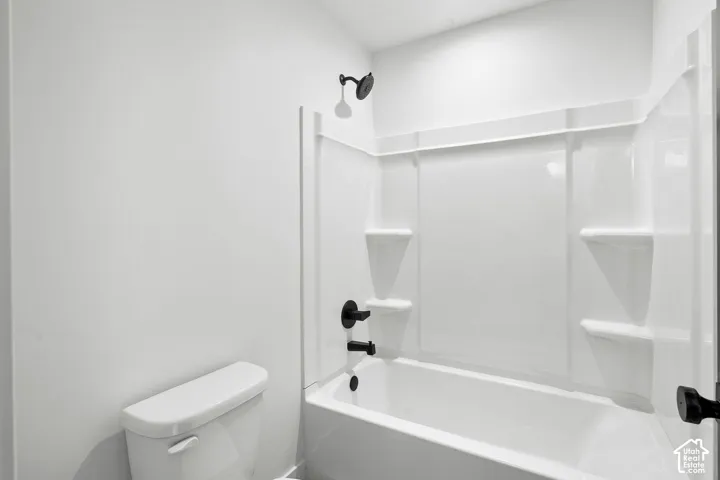 Bathroom featuring a white tub-shower combination with integrated shelving, matte black plumbing fixtures, and a white toilet