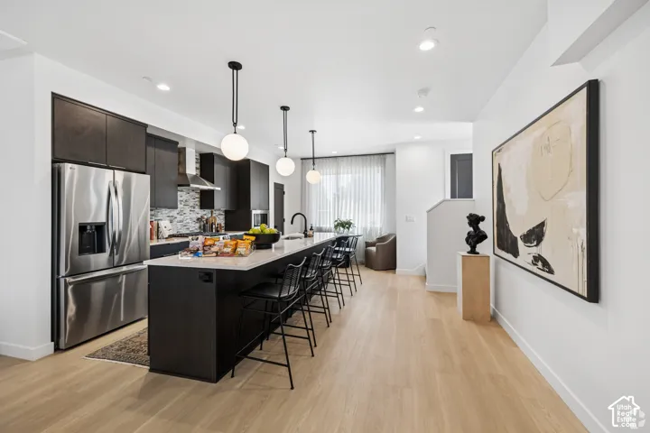 Kitchen featuring dark wood cabinetry, quartz countertops, a kitchen island with pendant lighting, stainless steel appliances, and wood-finish flooring