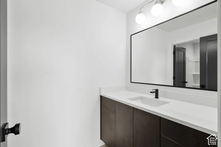Vanity featuring dark wood cabinetry, solid surface countertop with an integrated sink, matte black faucet, full-width mirror with black frame, and three-globe light fixture