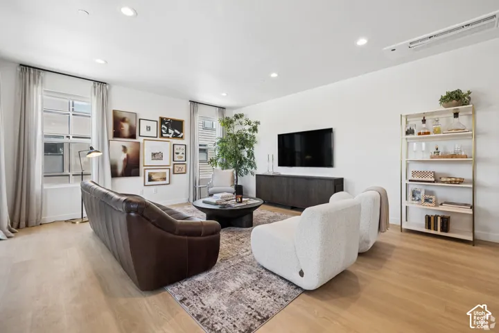 Open-concept living space featuring wood-finish flooring, recessed lighting, and large windows with integrated ceiling-mounted climate control