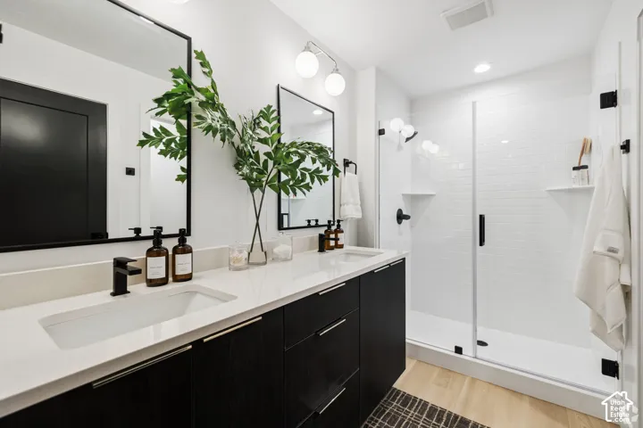 Double vanity with light-toned countertops and matte black fixtures, dark-finish cabinetry, rectangular under-mount sinks, framed vanity mirrors, and a glass-enclosed shower with white tile surround