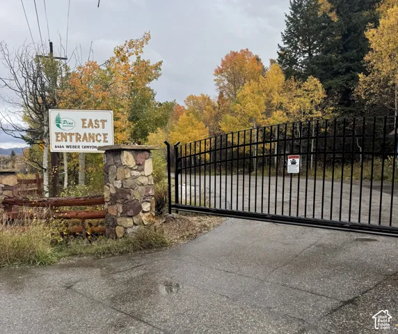 Gated entrance featuring stone masonry pillars and black metal fencing surrounded by mature deciduous trees