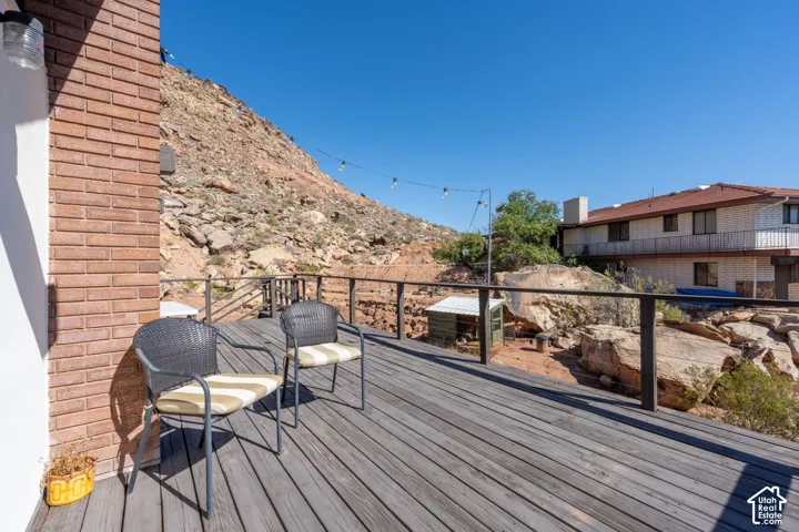 Elevated wood-plank deck featuring a metal railing and a backdrop of natural rock formations