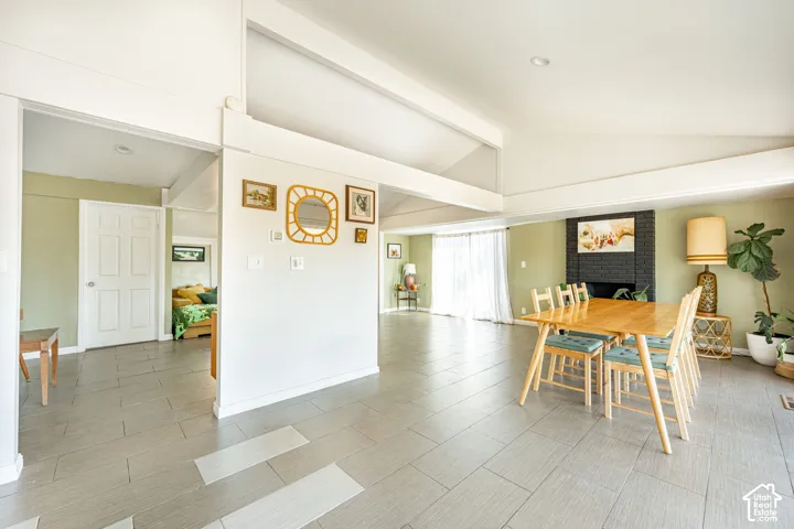 Vaulted ceilings with exposed structural beams, tile flooring, and a floor-to-ceiling brick fireplace