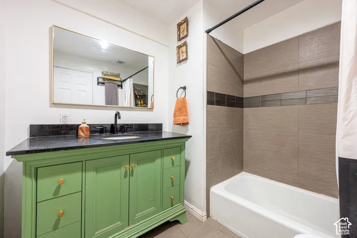 Bathroom vanity featuring a green cabinetry base, dark stone countertop with an integrated basin, and black faucet hardware, complemented by a shower enclosure with textured tile wall surfacing and a horizontal accent border
