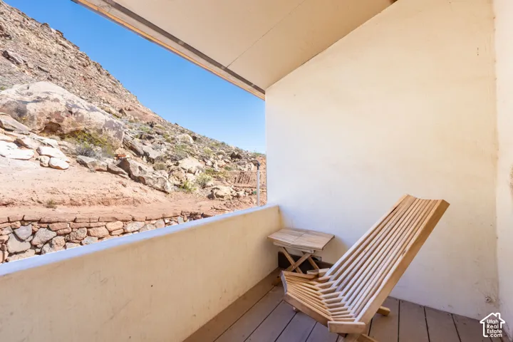Covered balcony off primary featuring smooth stucco walls, wood-finish flooring, and a stone-retaining wall exterior backdrop