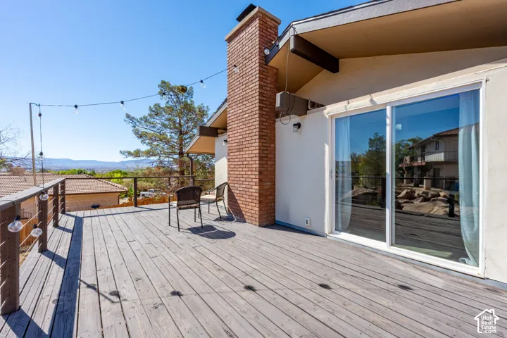 Expansive wooden deck featuring a brick chimney, cable railing, and sliding glass door access