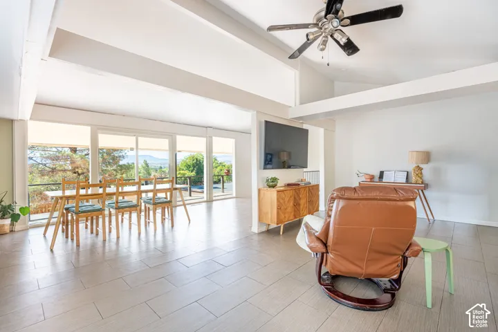 Vaulted ceilings with exposed structural beams, floor-to-ceiling sliding glass doors, tile flooring, and a ceiling fan with integrated lighting