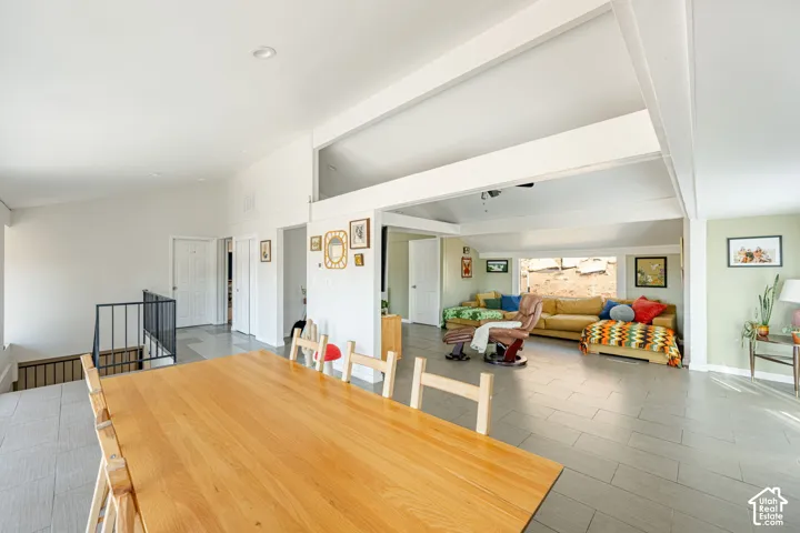 Open-concept interior featuring vaulted ceilings, exposed structural beams, tile flooring, and metal staircase railing