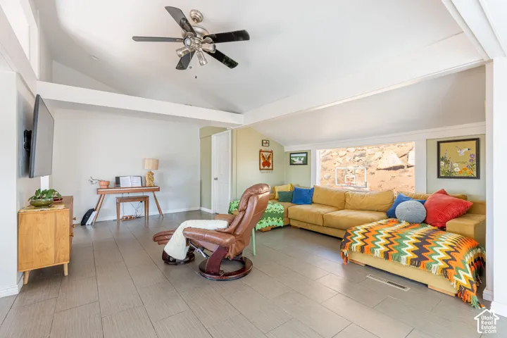 Vaulted ceilings, expansive ceramic tile flooring, and a large horizontal window with natural rock landscape exposure, featuring a built-in ceiling fan with integrated lighting