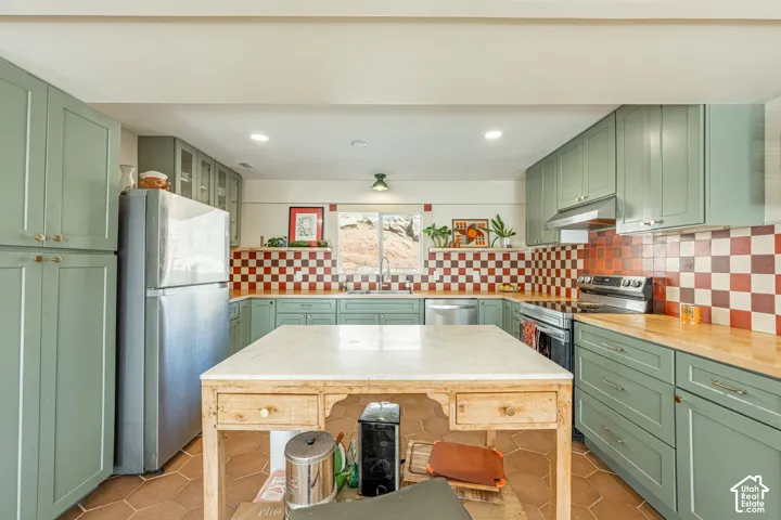 Kitchen featuring sage green cabinetry, stone-topped central island, checkerboard tile backsplash, wood-finish countertops, and hexagonal tile flooring