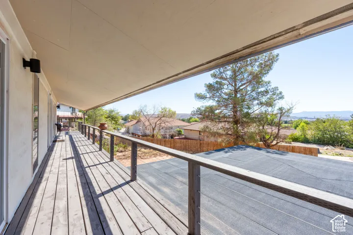 Covered wooden balcony with horizontal cable railing and wall-mounted exterior lighting