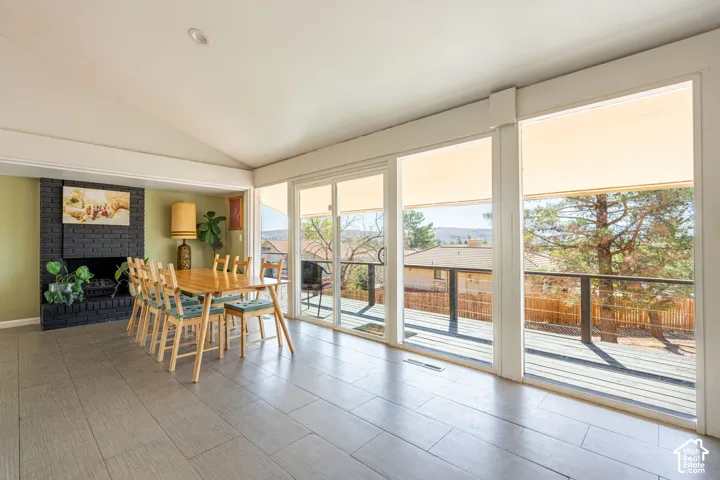Vaulted ceiling, floor-to-ceiling glass sliding doors, dark brick fireplace, and large-format tile flooring
