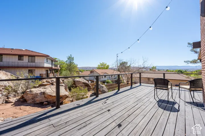 Elevated deck featuring gray wood-finish decking, metal railing with horizontal cable infill, and string lighting