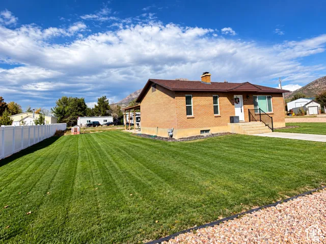 Single-story brick exterior residence featuring a covered patio, masonry chimney, white vinyl perimeter fencing, and mountain backdrop