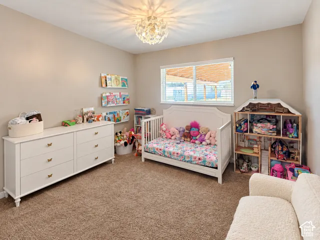 Neutral-toned bedroom featuring textured carpeting, a decorative multi-bulb flush-mount light fixture, and a large horizontal window