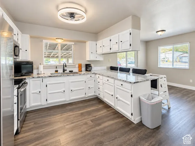Kitchen featuring white cabinetry, stone-finish countertops, stainless steel appliances, a matte black kitchen faucet, and wood-finish flooring