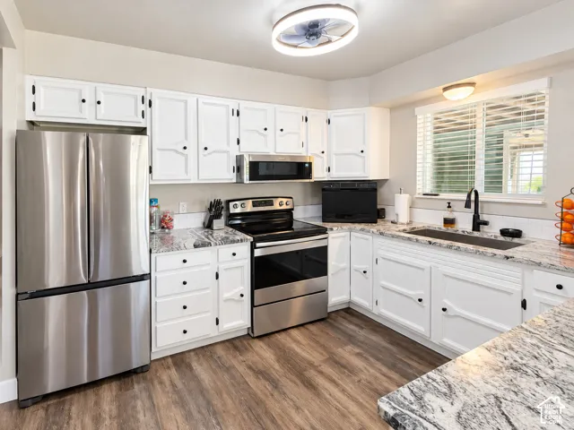 Kitchen featuring white cabinetry with black hardware, stone-finish countertops, stainless steel appliances, wood-finish flooring, and a matte black faucet