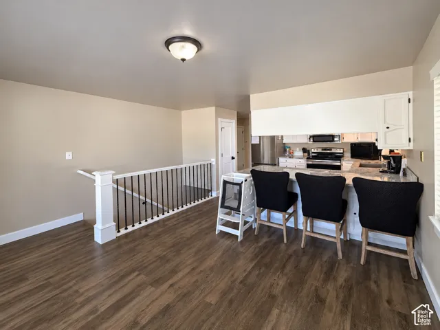 Kitchen featuring white cabinetry, stone-finish countertops, stainless steel appliances, and a breakfast bar, complemented by wood-finish flooring and a staircase with a white post and black metal balusters