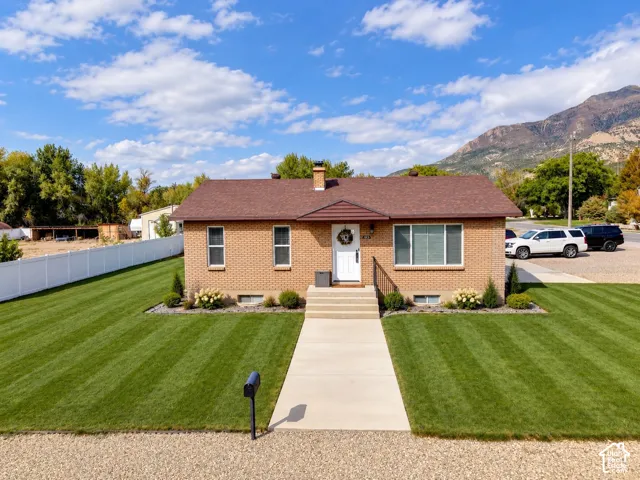 Single-story brick exterior featuring a shingled roof, mountain backdrop, concrete walkway, and manicured lawn