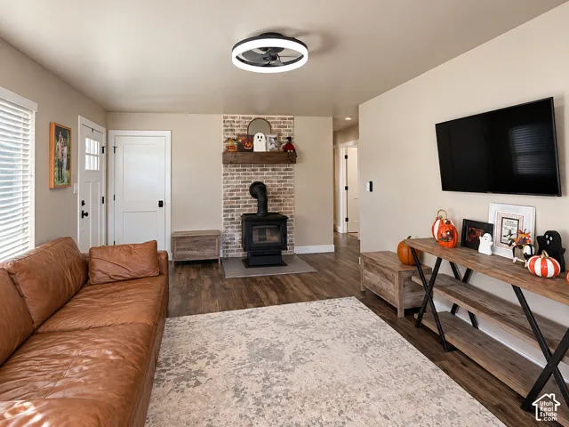 Living area featuring a brick-surround wood-burning stove with a timber mantel, wood-finish flooring, and a modern circular flush-mount light fixture