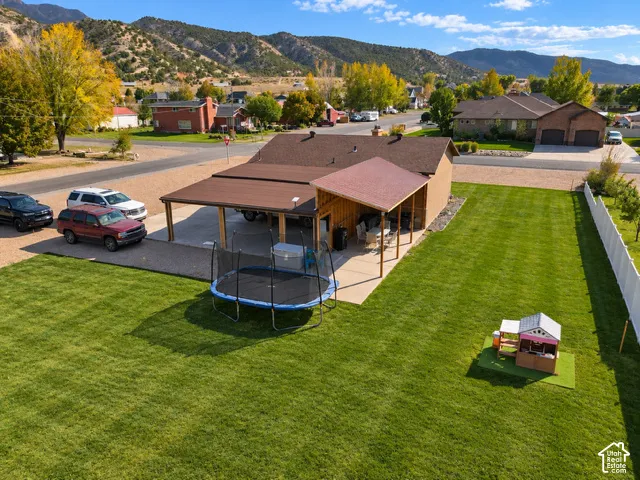 Expansive lawn area featuring a covered concrete patio, wood-post structural supports, and mountain backdrop