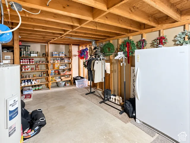 Storage area featuring exposed ceiling joists, concrete flooring, built-in wooden shelving, and a water heater