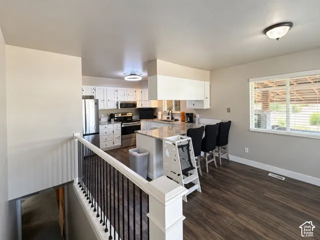 Kitchen and dining area featuring wood-finish flooring, white cabinetry, stainless steel appliances, and a kitchen island with seating