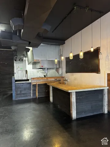 Industrial-style space featuring exposed metal ductwork, a custom wood-paneled service counter, stainless steel commercial hood, and decorative glass pendant lighting and an open kitchen concept