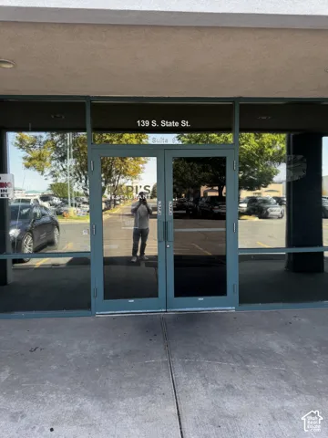 Commercial storefront entrance featuring expansive floor-to-ceiling plate glass windows, double glass doors with metal framing, and a covered concrete walkway