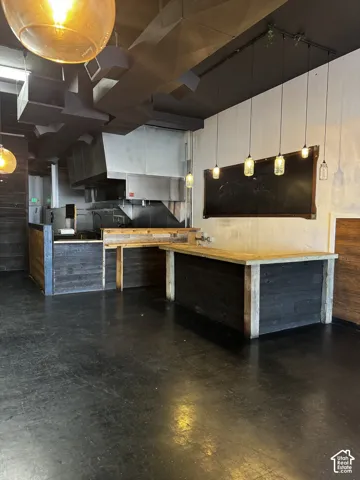 Industrial interior featuring a charcoal-finished exposed ceiling with metal ductwork, custom dark-stained wood-paneled service counters, and decorative hanging pendant lighting