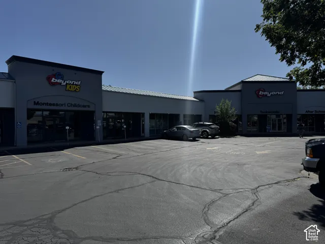 Commercial exterior featuring a paved parking area and multi-tenant storefronts with metal roofing