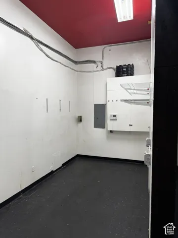 Utility space featuring dark-finish flooring, white walls, a red-painted ceiling, integrated white cabinetry with shelving, and exposed electrical conduits