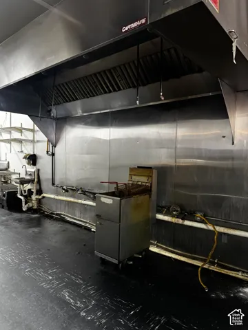Commercial kitchen workspace featuring a stainless steel CaptiveAire ventilation hood, wall-mounted stainless steel backsplash, and a dedicated prep sink