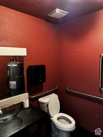 Restroom featuring a glass vessel sink, dark countertop, white toilet, and multiple stainless steel grab bars