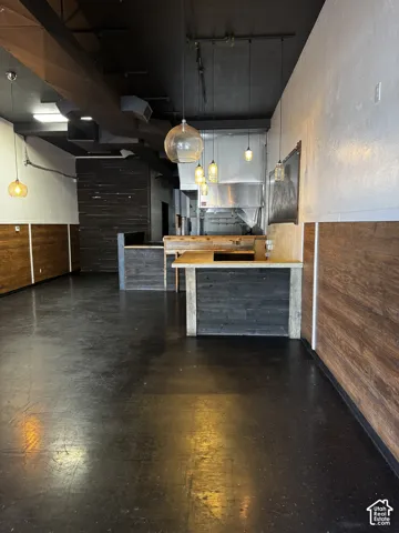 Open-concept commercial space featuring high exposed ceilings, dark polished flooring, wood-paneled walls, custom-built counter, and integrated stainless steel hood system