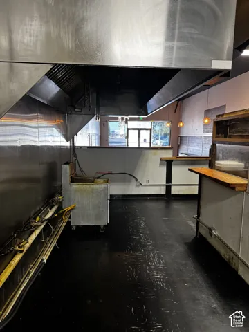 Commercial space featuring a stainless steel exhaust hood, built-in service counter with wood-finish top, hard-surface flooring, and pendant lighting