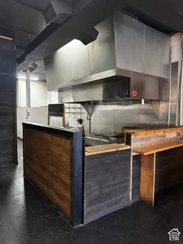 Commercial kitchen area featuring a stainless steel ventilation hood, stainless steel backsplash, and wood-paneled service counter with a built-in wooden ledge