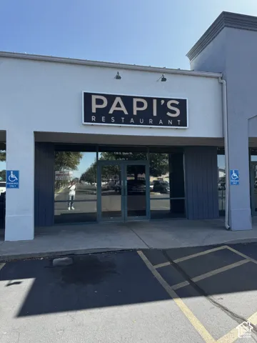 Commercial storefront featuring a stucco exterior, expansive glass-front facade, integrated signage lighting, and concrete paved entrance