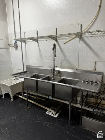 Commercial-grade stainless steel triple-basin sink featuring a high-arc pull-down sprayer faucet, integrated side drainboards, mounted wire shelving, and a secondary utility basin