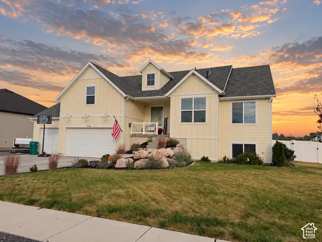 Board-and-batten exterior with a multi-gabled roofline, front porch featuring white railing, integrated multi-car garage, and tiered stone landscaping
